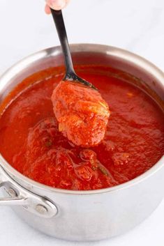 someone is spooning tomato sauce into a pot with meatballs in it on a white surface