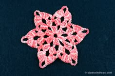 a pink crochet snowflake sitting on top of a black tablecloth