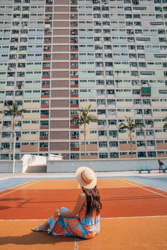 a woman sitting on top of a tennis court next to a tall building with balconies