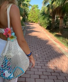 a woman walking down a brick road carrying a mesh bag with flowers on the side