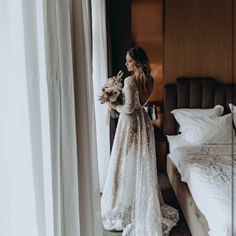 a woman standing in front of a bed holding a bouquet of flowers and looking out the window