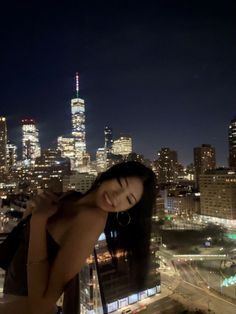 a woman standing on top of a building in front of a cityscape at night