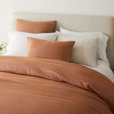 an unmade bed with two pillows on top of it and a plant in the corner