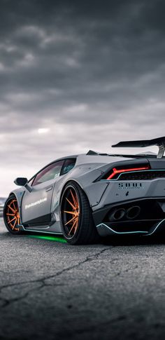 a white sports car with orange rims parked on the street in front of dark clouds