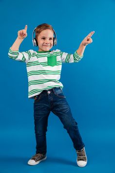 a young boy wearing headphones and holding his arms in the air while standing against a blue background