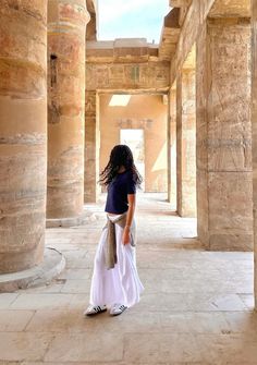 a woman standing in an ancient building looking at the ceiling and columns that are all lined up