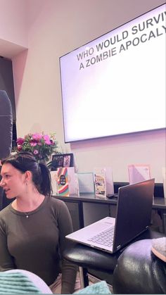 two women sitting in front of a laptop computer on top of a desk with a projector screen behind them