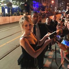 a woman in a black dress signing autographs for fans on the street at night