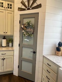 a kitchen with white cabinets and gray door, along with a windmill on the wall