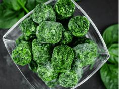 a glass bowl filled with green vegetables on top of a black table next to basil leaves