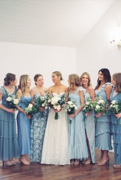 a group of women standing next to each other in front of a white wall holding bouquets