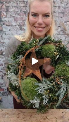 a woman holding a wreath with moss and pine cones