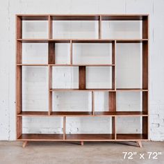 a wooden bookcase sitting on top of a cement floor next to a white brick wall