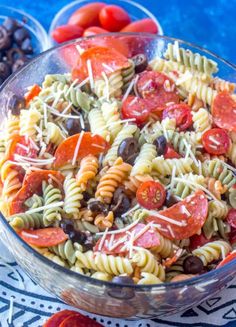 a glass bowl filled with pasta salad next to tomatoes and olives