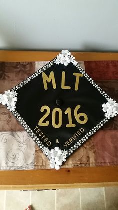 a decorated black and gold graduation cap with the words mtt 2016 on it, sitting on top of a table