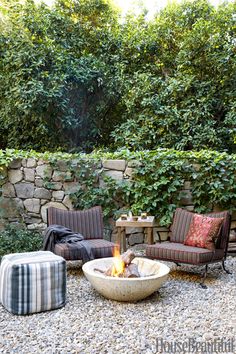 an outdoor fire pit surrounded by chairs and tables next to a stone wall with ivy growing on it