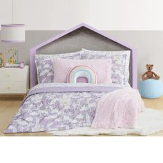 a child's bed with pink and purple comforter, pillows and stuffed animals