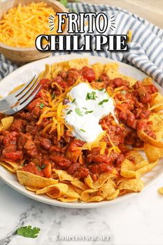 a white plate topped with nachos covered in chili and cheese next to a bowl of shredded cheese