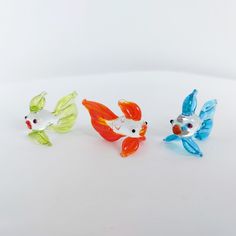 three small glass fish sitting next to each other on a white surface with one goldfish in the middle