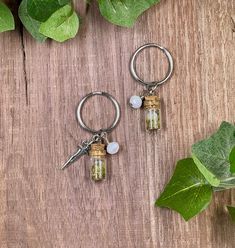 two key chains with small glass bottles attached to them on a wooden table next to leaves