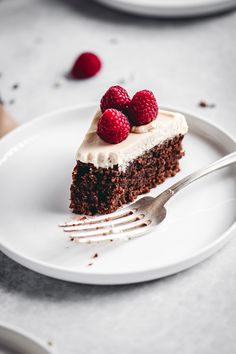 a piece of cake on a white plate with raspberries