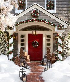 a red door is decorated with christmas wreaths and lights in front of a house