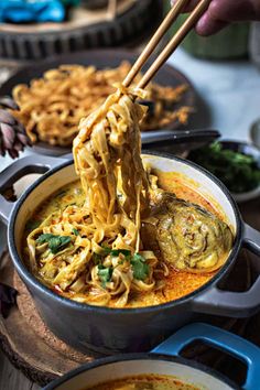 someone is holding chopsticks over noodles in a pot