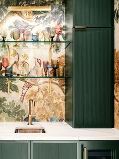 a kitchen with green cabinetry and wallpaper on the walls, along with a stainless steel sink