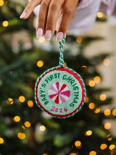 a woman's hand holding a christmas ornament in front of a tree