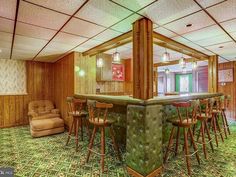 a bar with chairs and stools in a room that has wood paneling on the walls