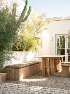 an outdoor table and benches in front of a house with cactus trees on the side