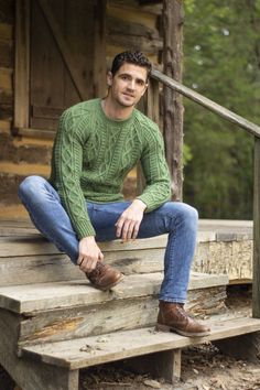 a man sitting on some steps wearing a green sweater and blue jeans with brown shoes