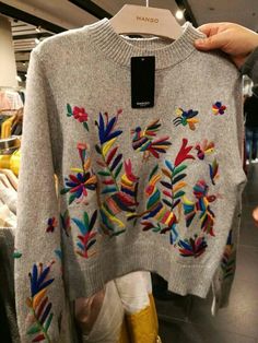 someone is holding up a sweater that has been decorated with multicolored flowers and leaves