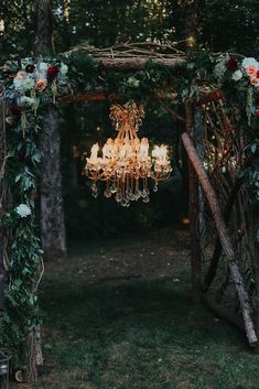 a chandelier hanging from a wooden structure in the middle of a forest with flowers and greenery