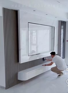 a man kneeling down in front of a flat screen tv on a wall mounted to the side of a white cabinet