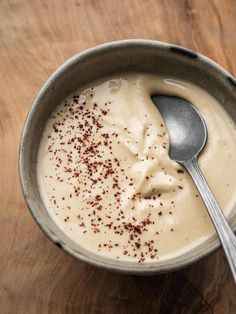 a spoon in a bowl filled with cream and brown sprinkles on top of a wooden table