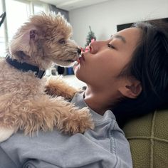 a woman laying on a couch kissing a dog with her nose close to her face