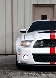 a white mustang with red and white stripes parked in front of a metal building,