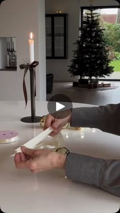 a woman is cutting paper with scissors on a table in front of a christmas tree