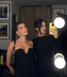 two women standing next to each other in front of a mirror holding up their cell phones