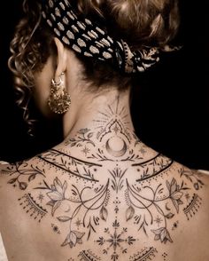 the back of a woman's neck is adorned with intricate tattoos and an ornate headband