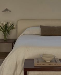 a bowl on a table in front of a bed with white linens and pillows