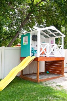 a small play house with a slide in the grass next to a white picket fence