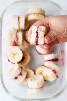 a hand holding a half eaten banana with raspberry jam on it in a glass dish