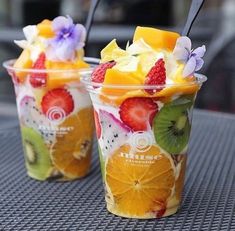 two plastic cups filled with fruit and ice cream on top of a metal table next to each other