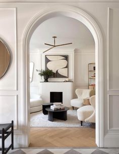 a living room with an arch leading into the dining room and sitting area that is decorated in white