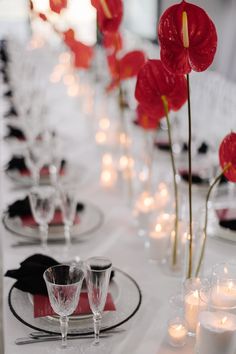 the table is set with white and red place settings, candles and flowers in vases