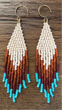 the beaded earrings are hanging from hooks on a wooden surface, with blue and orange beads