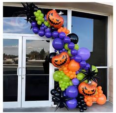 a halloween balloon arch decorated with pumpkins, bats and spider web balloons in front of a building