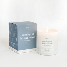 a candle sitting next to a box on a white surface with the words morning at the lake house printed on it